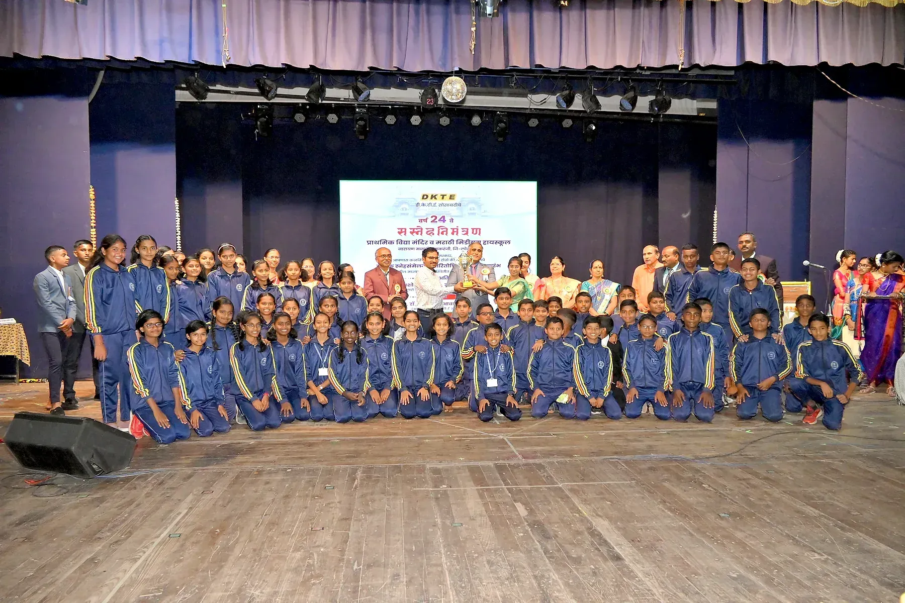 A large group of uniformed schoolchildren and guests photographed on stage