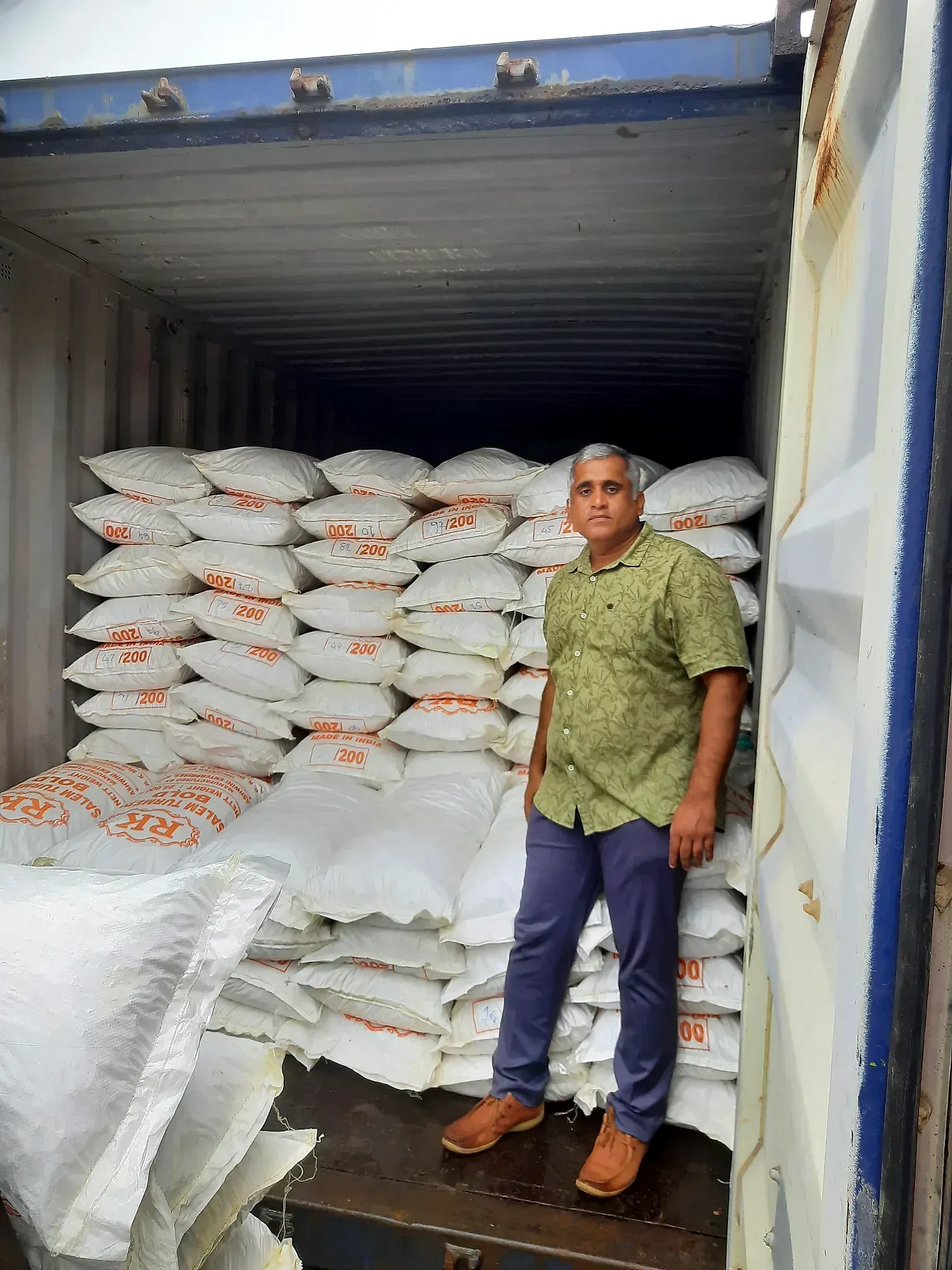 A man standing in front of sacks stacked to the roof inside a container bound for Malaysia