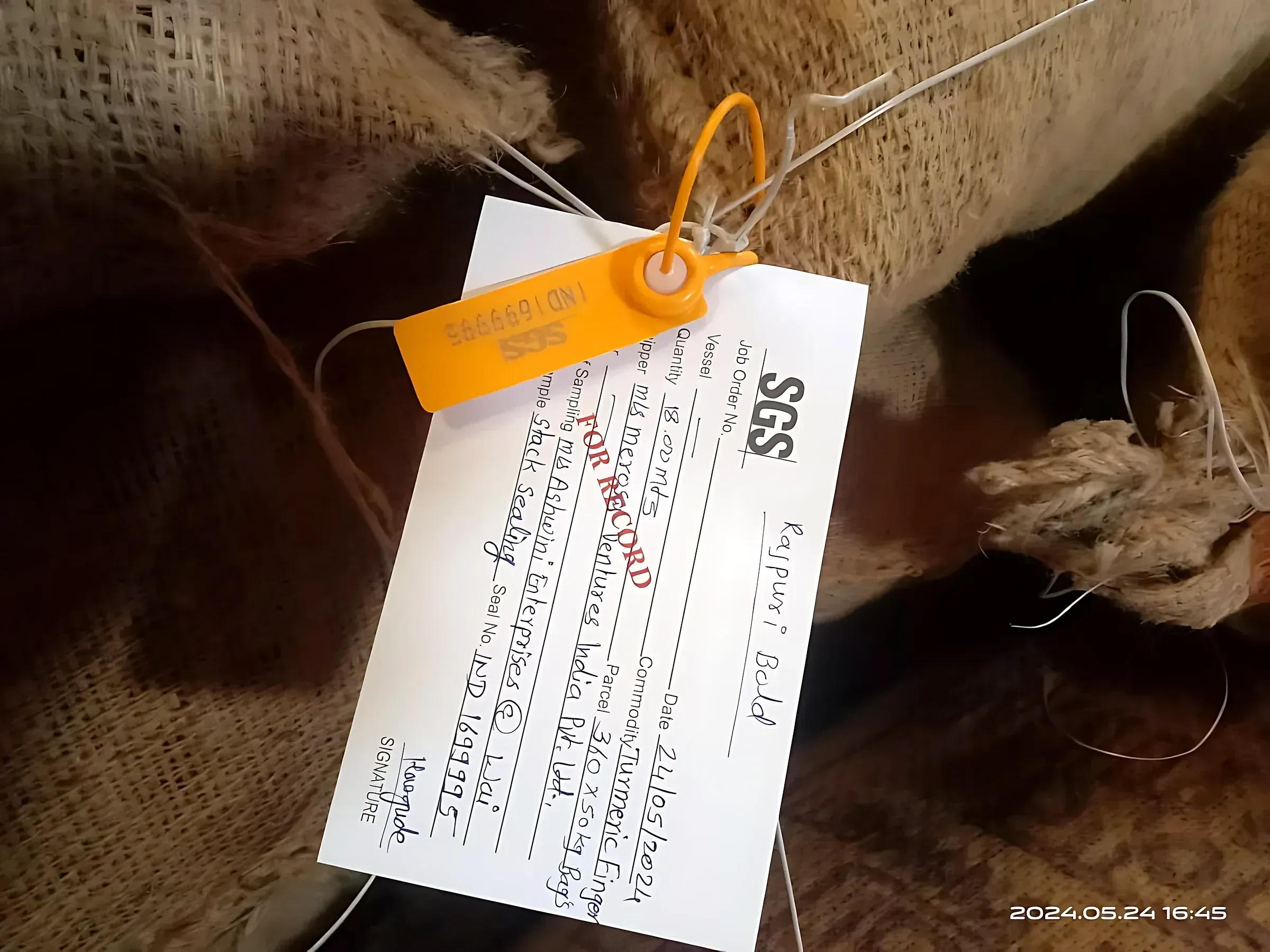 An SGS inspection tag and numbered orange seal fastened to a jute bag, recording the commodity and bag count